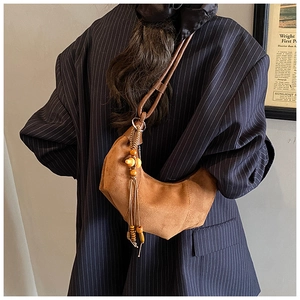 Detail of a brown suede crescent hobo bag with knotted strap and wooden bead tassels