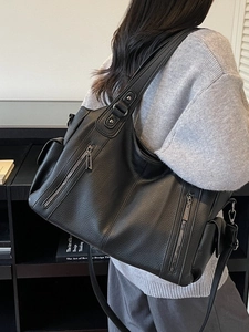 Large black pebbled leather tote bag with double zippers worn as an underarm shoulder bag