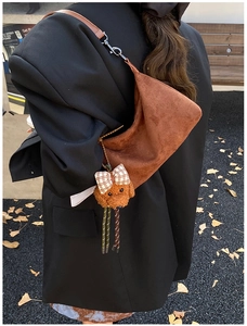 Détail du sac croissant en daim avec breloque chiot sur un blazer en laine noire
