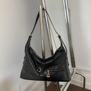 Detail of black wrinkled patent leather tote with gold zipper and round metal pendant
