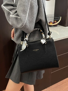Elegant black pebbled leather tote bag with decorative silk scarf and gold brand logo