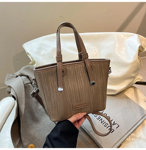 Detail of brown woven texture tote bag with leather logo stamp and adjustable shoulder strap