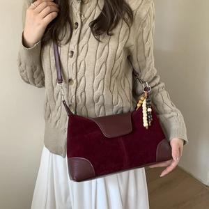 Detail of burgundy suede crossbody bag with decorative wooden bead tassel charm