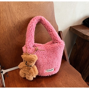 Détail d'un sac seau en peluche rose avec un pendentif ours et une étiquette tissée