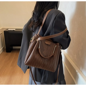 Detail of dark brown woven bucket bag with U-shaped metal handle and adjustable strap