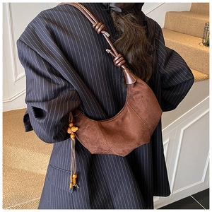 Detail of dark brown suede half-moon crossbody bag with knot strap and wooden bead tassels