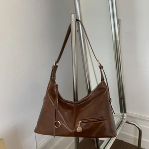 Close-up of brown glossy leather dumpling bag with metal pendant and zipper detail