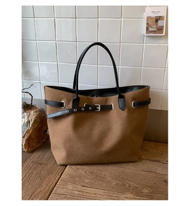 Detail of dark brown tote bag with leather buckle strap on vintage wood table