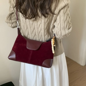 Detail of burgundy faux suede shoulder bag with beaded charm and adjustable strap