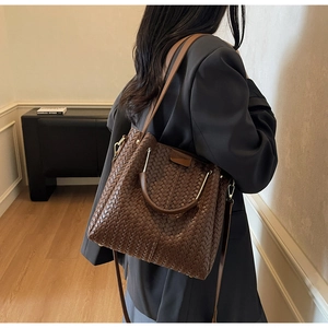 Detail of dark brown woven texture tote bag worn by model in a soft indoor setting