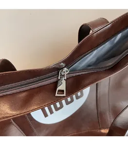 Detail of smooth metal zipper and silver puller on dark brown faux leather tote bag