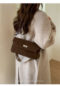 Close-up of a vintage dark brown suede crossbody bag with a metallic twist lock on a model