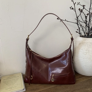 Close-up of vintage burgundy oily leather texture and metal zipper detail on hobo bag