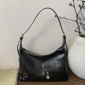 Detail of black wrinkled patent leather shoulder bag with gold zipper on a wooden table