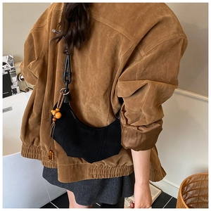 Close-up of black crescent hobo bag with wood bead charm on brown suede jacket