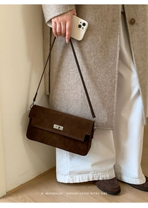 Brown suede crossbody bag paired with a beige wool coat and white trousers in a minimal setting
