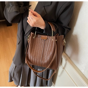 Detail of a brown woven bucket bag with leather handles and gold metal hardware