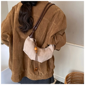 Detail of beige suede hobo bag with wood bead tassel and dark brown leather strap