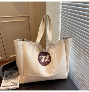 Detail of cream tote bag with red circular logo and laptop in soft indoor light