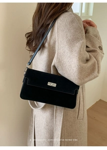 Detail of a minimalist black suede shoulder bag with a silver metallic twist-lock buckle