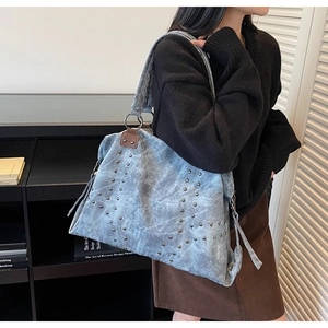 Détail de clous argentés et glands décoratifs sur sac cabas en cuir bleu lavé