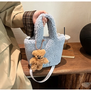 Détail d'un sac seau en peluche bleu clair avec breloque ours brun et large bandoulière