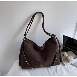 Detail of dark brown tote bag showing matte texture and decorative side metal buckles