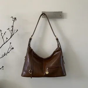 Detail of vintage brown leather hobo bag featuring polished oil wax texture and zip pocket
