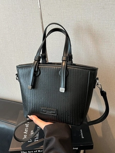 Black woven bucket bag with top handles and leather shoulder strap on a book background