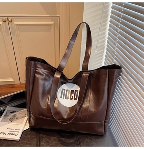 Detail of dark brown leather tote bag with NOCO logo in a warm interior setting