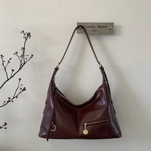 Detail of burgundy waxed leather dumpling bag with gold hardware and side zipper pocket