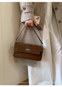 Detail of a brown suede shoulder bag featuring a silver twist lock and minimalist retro design