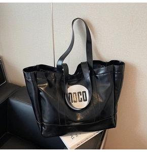 Detail of black tote bag with white MOCO logo on a leather sofa in modern studio