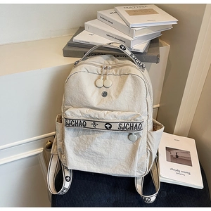 Detail of cream nylon backpack featuring pleated texture and front zipper pocket