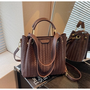 Detail view of deep brown woven leather bag texture and rounded top handle on a table