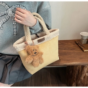 Detail of yellow tote bag with fuzzy white fleece handle and a brown plush bear charm