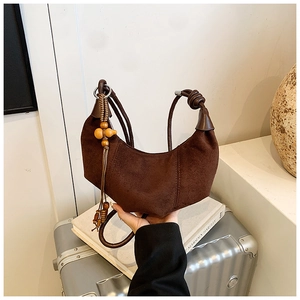 Detail of suede crossbody bag with knot handle and decorative wooden bead tassel