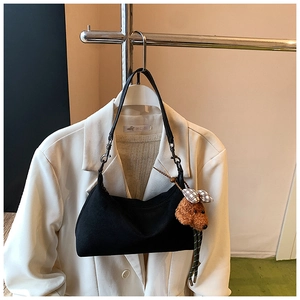 Détail du sac dumpling noir en suède avec pendentif chiot marron sur un blazer ivoire