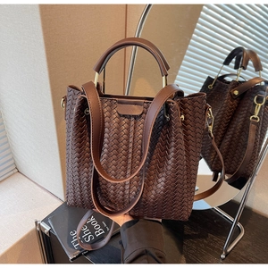 Detail of dark brown woven leather texture and metal handle buckle on a bucket bag