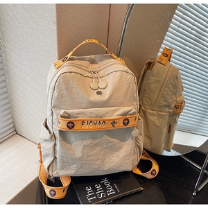 Detail of beige nylon backpack featuring orange woven strap with blue floral embroidery