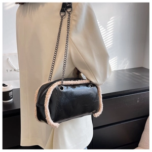 Detail of black glossy leather crossbody bag with cream plush trim and silver chain strap