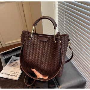 Detail of dark brown woven leather bucket bag with gold ring handle and metal hardware
