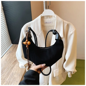 Detail of black suede crescent bag with woven handle and wooden gourd tassel accessory