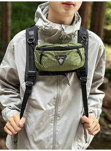 Nahaufnahme der grünen Gittertasche mit Logo an einem Rucksackgurt im Freien