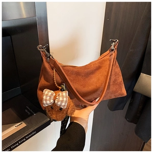 Détail du sac à bandoulière en daim marron avec une breloque chien en peluche et nœud