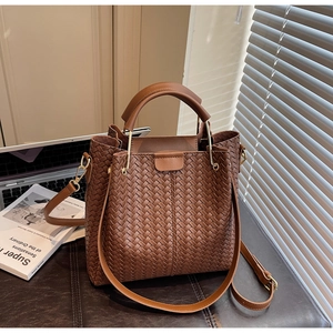 Detail of dark brown woven leather bucket bag with golden hardware on a desk