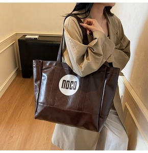 Close-up of a large dark brown tote bag with NOCO logo carried by a model in a trench coat