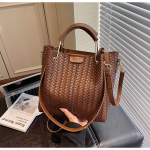 Detail of dark brown woven leather bucket bag with gold hardware and shoulder strap