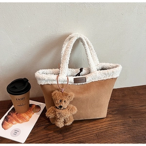 Detail of suede tote bag with faux shearling handles and cute bear charm on desk