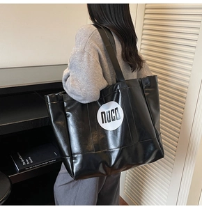 Detail of spacious black glossy tote bag with noco logo being worn by a model